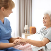 Caregiver massaging hand of senior woman at home