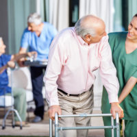 Happy Caretaker Assisting Senior Man In Using Zimmer Frame Happy Caretaker Assisting Senior Man In Using Zimmer Frame