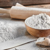 Bowl of flour and rolling pin on wooden background