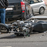 broken motorcycle closeup beside the car. an accident on the road in the city on a sunny day involving a motorcycle and a car.