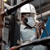 African mechanical supervisor in safety mask doing inspection on plant. African mechanical supervisor in safety mask doing inspection on plant.