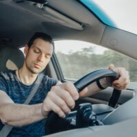 Fatigue of sleeping driver driving at speed while holding wheel while driving on highway in forest. Front view of exhausted man