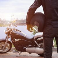 Biker holding helmet with motorcycle on sunset.