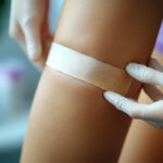 A clean and sterile bandage being applied to a small wound on a person's knee. A clean and sterile bandage being applied to a small wound on a person's knee.